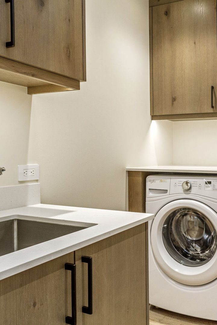 A close-up of a laundry room with a sink and brown cabinet.