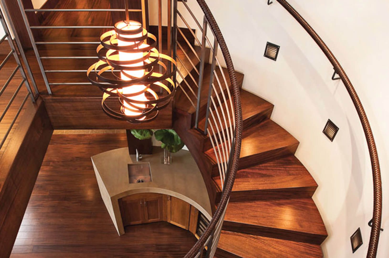A close-up of a spiral staircase, a wooden floor below, and a chandelier.