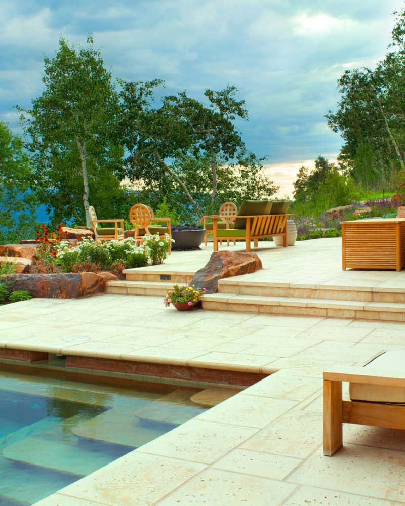 A wide shot of a lounge area with a brown bench and a pool against a cloudy sky and trees in the background.