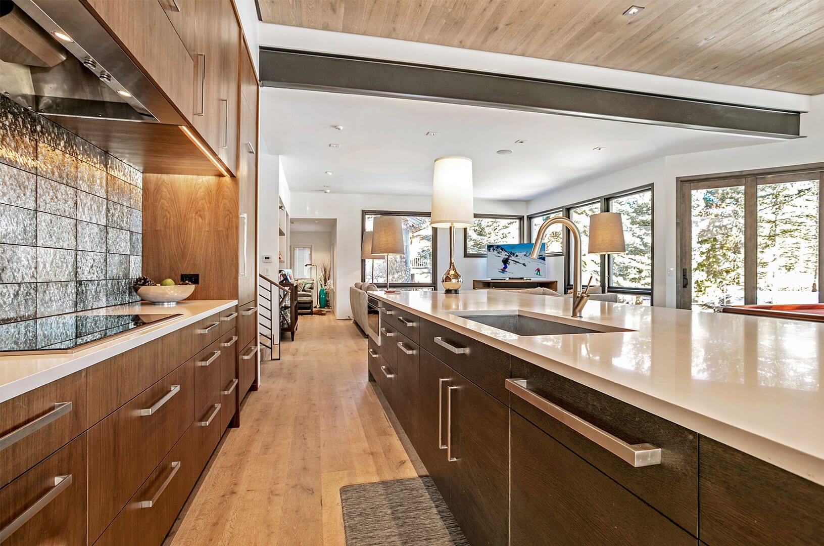 A full shot of a modern kitchen with a kitchen sink, lampshades, a wooden floor, and a wooden cabinet.
