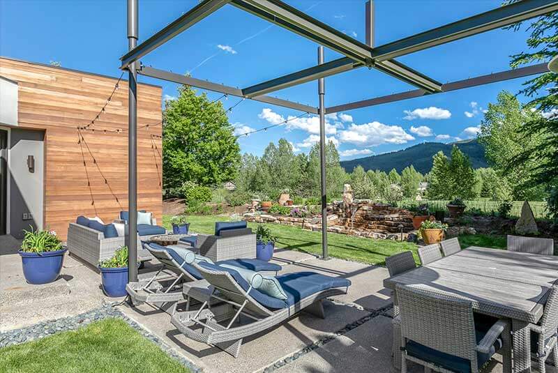 A wide shot of the exterior lounge with a blue and gray bench and a gray dining set with trees and mountain views A wide shot of Buckboard Road's exterior view